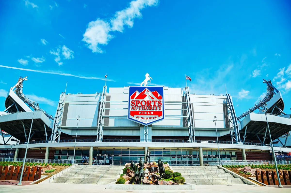 The image showcases Sports Authority Field at Mile High, emphasizing the stadium's bold signage, impressive architecture, and surrounding landscaping. The excitement around the venue is palpable, suggesting the energy of a game day or special event. The clear view creates a sense of anticipation and highlights Denver’s vibrant sports scene.