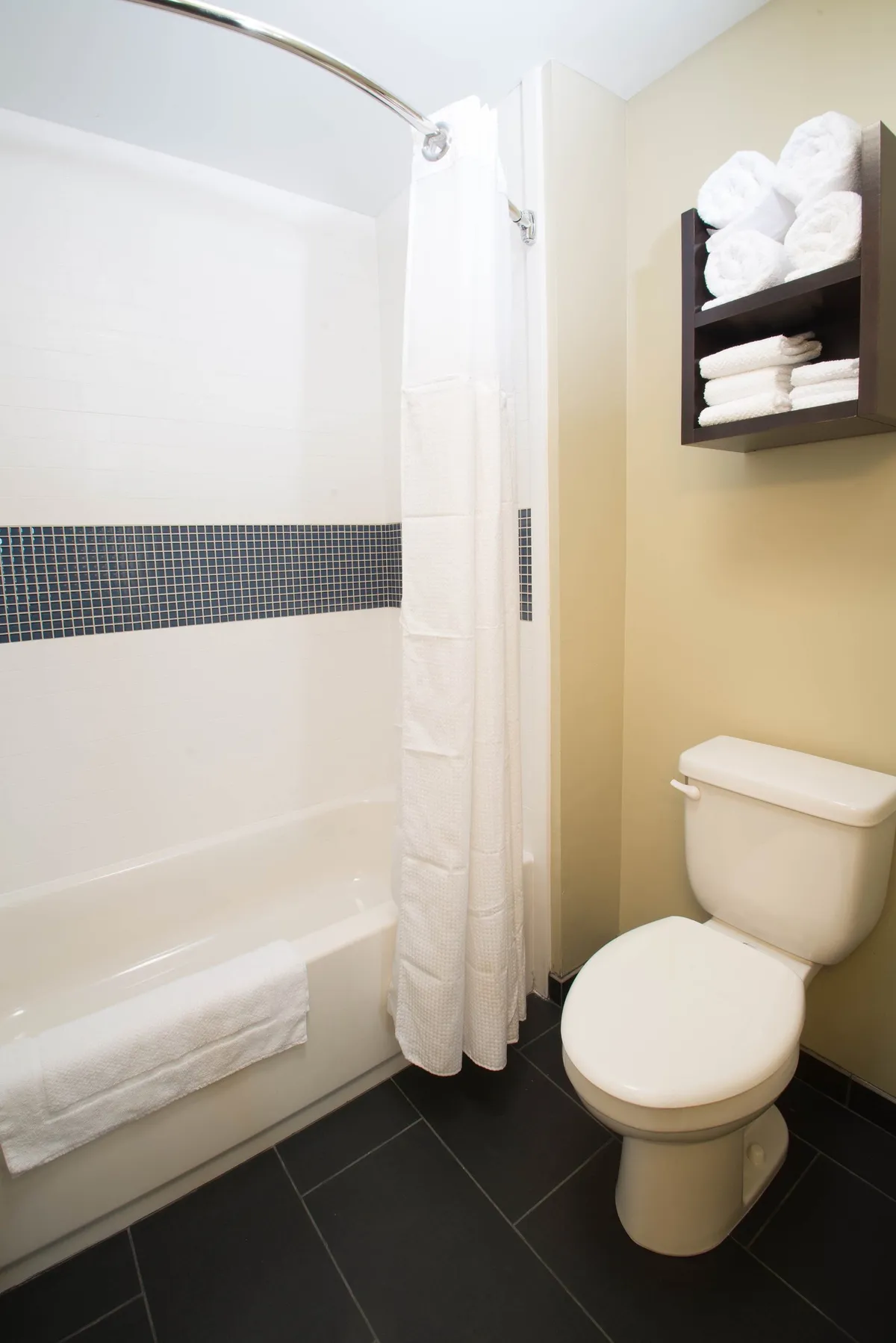 A modern bathroom is showcased, featuring a bathtub, shower curtain, and neatly arranged towels, suggesting a fresh, well-appointed space for self-care and relaxation.