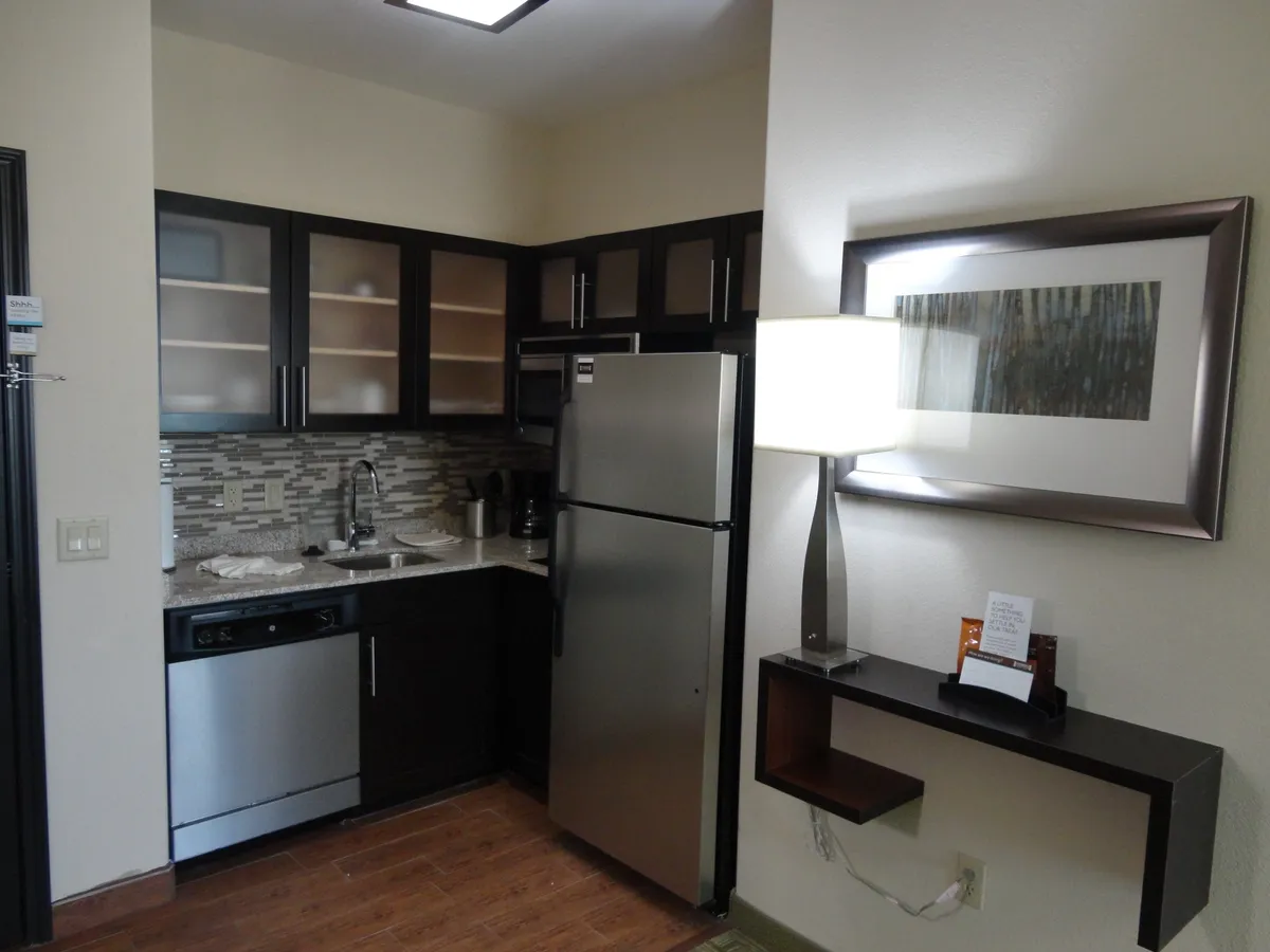 A contemporary kitchen space featuring a stainless steel refrigerator, sleek kitchen sink, modern lighting, and ample cabinetry. The scene hints at meal preparation or hosting, with a welcoming atmosphere suggesting the space is ideal for both cooking and social gatherings.